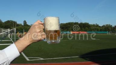一个男人`手拿着一杯<strong>啤酒</strong>，背景是一个足球场，在那里他们踢足球，特写镜头